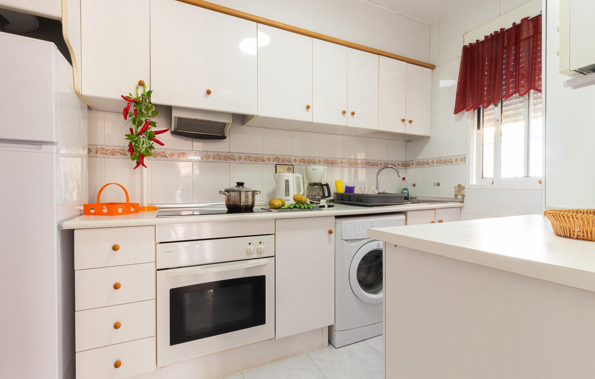 A modern kitchen with white cabinets, a built-in oven, a washing machine, and a coffee maker.