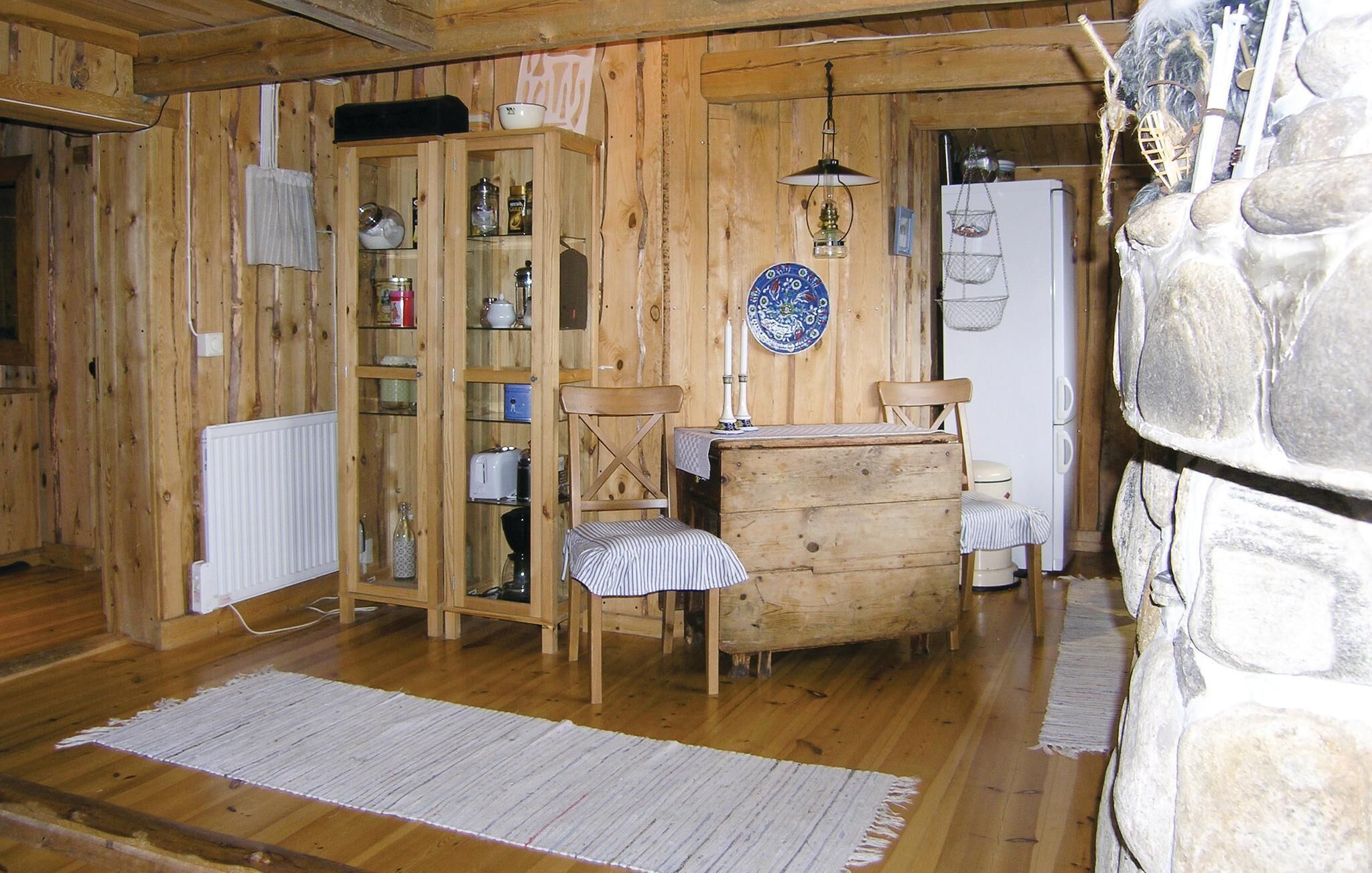 A rustic wooden room with a wooden cabinet, a table with chairs, a hanging light fixture, and a stone wall.