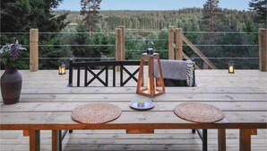 A wooden deck with a table, two woven placemats, a candle, a lantern, and a bench.