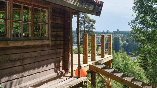A wooden cabin with a wooden deck and a view of a forested valley.