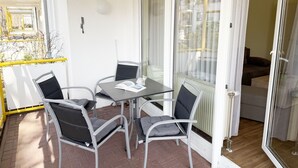 Un patio con una mesa y sillas, una puerta corrediza de vidrio que da a una habitación y una barandilla amarilla.