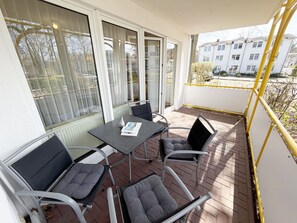 A balcony with a table and chairs, large windows, and a view of buildings.