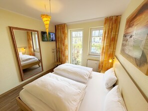 A hotel room with a bed, a television, a mirror, and a window with curtains.