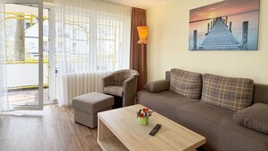 Una sala de estar con sofá, sillón, reposapiés y una mesita de centro con control remoto y flores.