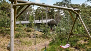 Un parc de balanços de fusta en una zona boscosa amb una petita cabana al fons.