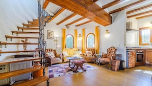 A spacious living room with a wooden staircase, two large windows with curtains, a fireplace, and a kitchen area. - Pet friendly home in Els Poblets (Els Poblets)