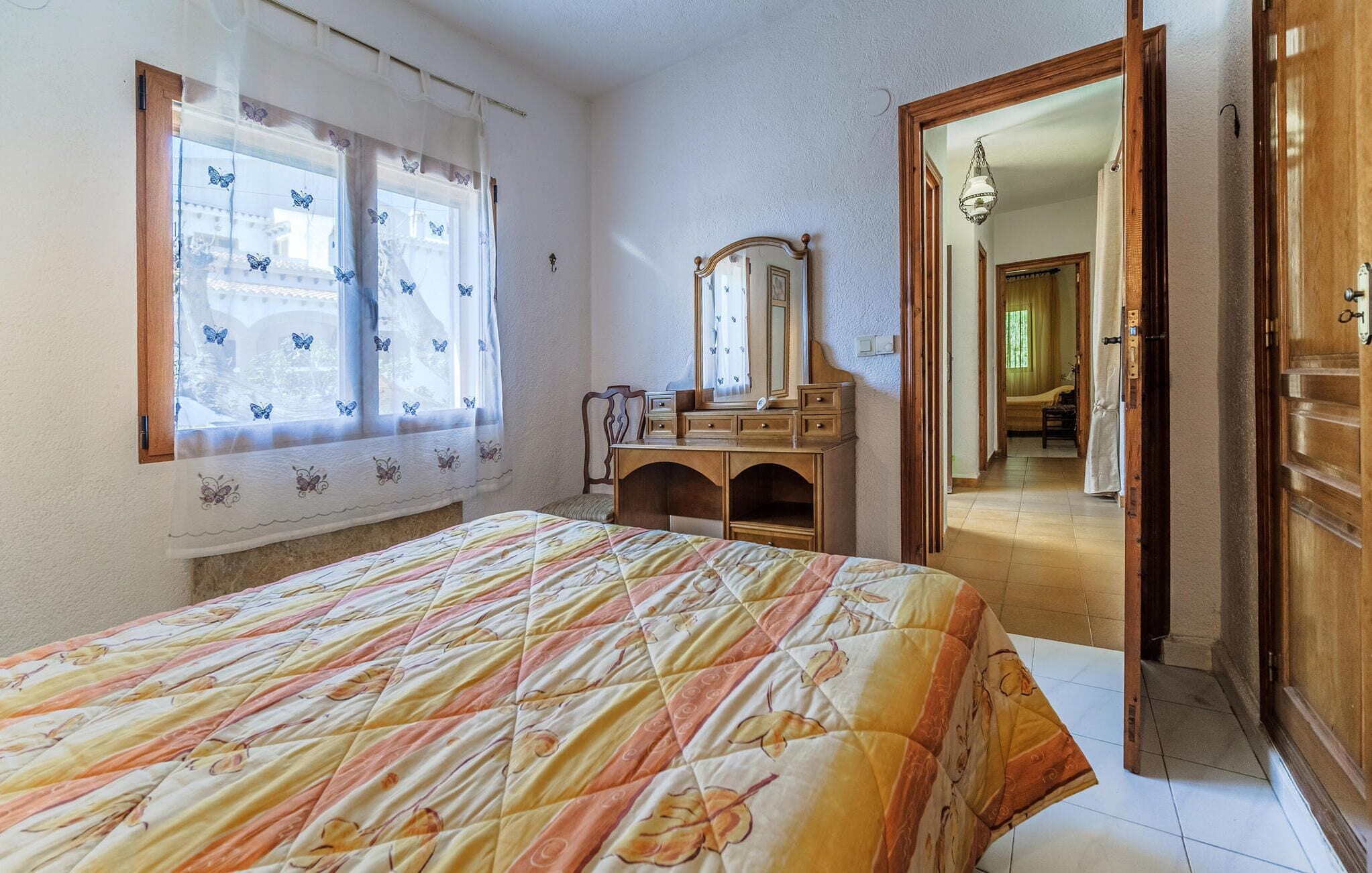 A bedroom with a bed, a dresser, a mirror, and a window with butterfly curtains.
