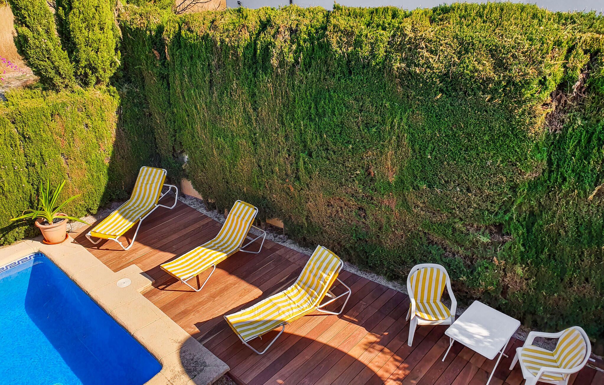 A poolside area with wooden decking, yellow-striped lounge chairs, and a white table.