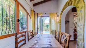 A dining area with a long table, wooden chairs, and a view of a pool through a glass door. - Pet friendly home in Els Poblets (Els Poblets)