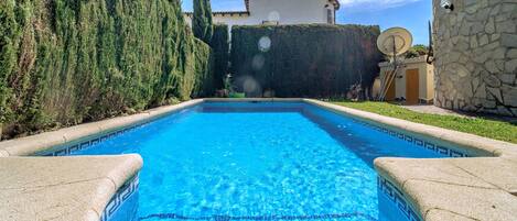 Una piscina rettangolare con piastrelle blu, circondata da un muro in pietra e un siepe.