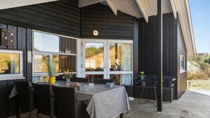 Un área de comedor al aire libre con mesa y sillas, una terraza de madera y vistas del paisaje circundante.