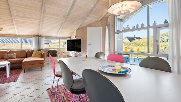 Una habitación acogedora con techo de madera, un ventanal con vistas al campo, una mesa de comedor con sillas y un televisor de pantalla plana.
