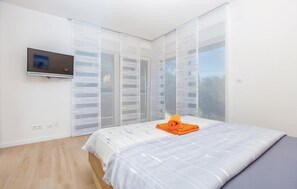 Une chambre à coucher avec un lit, un téléviseur fixé au mur et de grandes fenêtres équipées de stores.