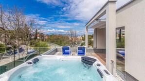 A hot tub with two blue lounge chairs, a glass balustrade, and a view of a residential area with houses and trees. - Gorgeous home in Malinska (Malinska)