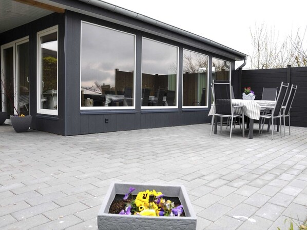 Ein modernes Haus mit großen Fenstern, einer Terrasse mit Tisch und Stühlen sowie einem Blumenkasten.