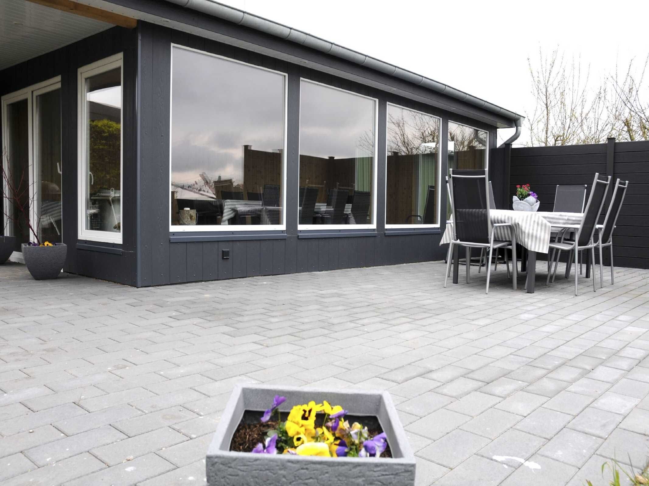 A modern house with large windows, a patio with a table and chairs, and a flower planter.