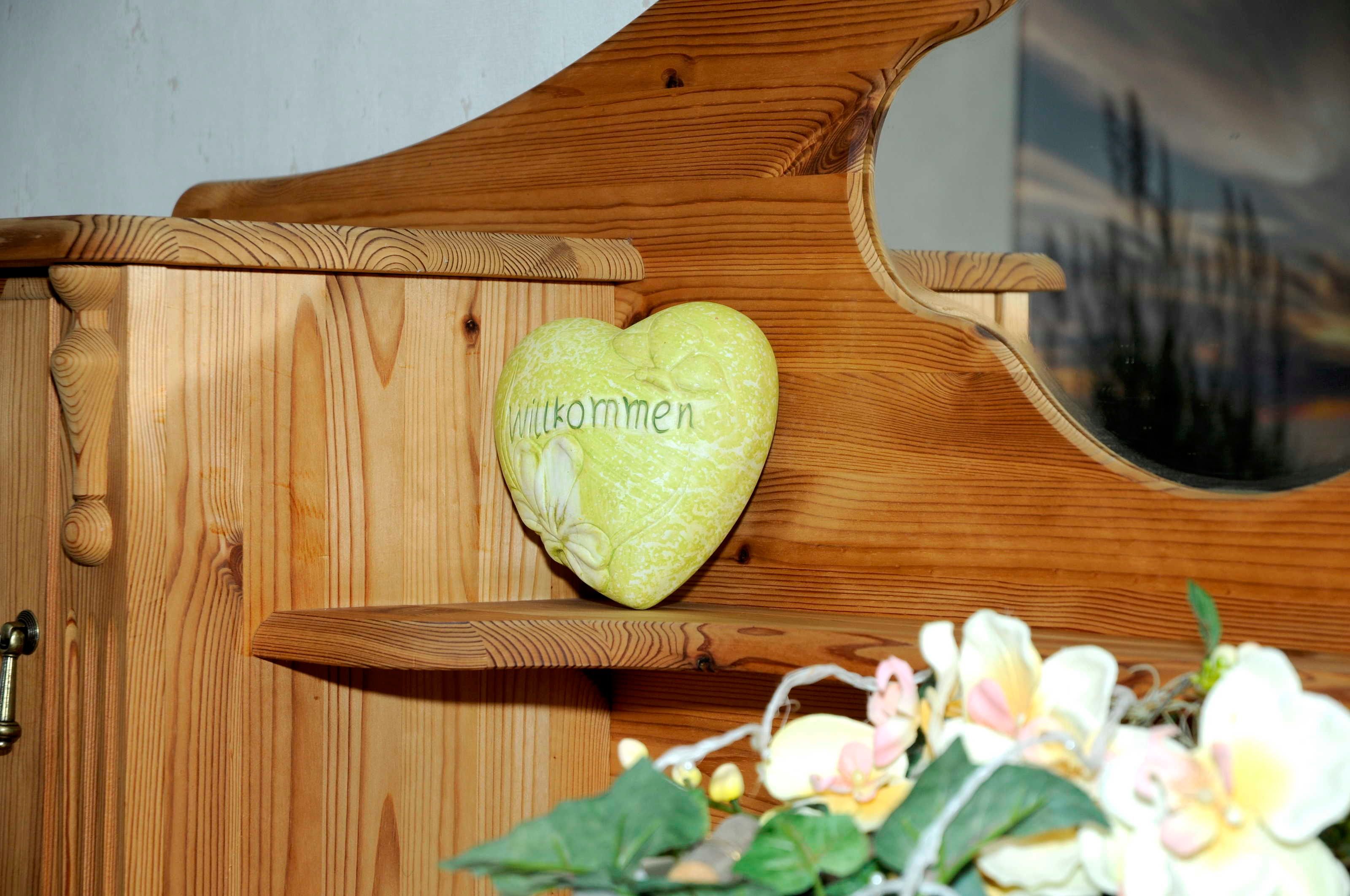 Un mobiletto in legno con un oggetto a forma di cuore e la scritta 'Willkommen'.