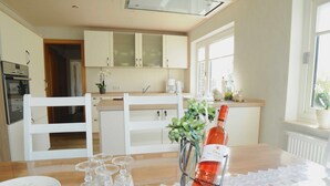 A kitchen with white cabinets, a wooden countertop, and a dining table with a lace table runner. - Vacation apartment Meer, Germany (Hasselberg)