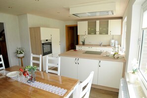 A modern kitchen with white cabinets, a wooden countertop, and a dining area with a table and chairs. - Vacation apartment Meer, Germany (Hasselberg)