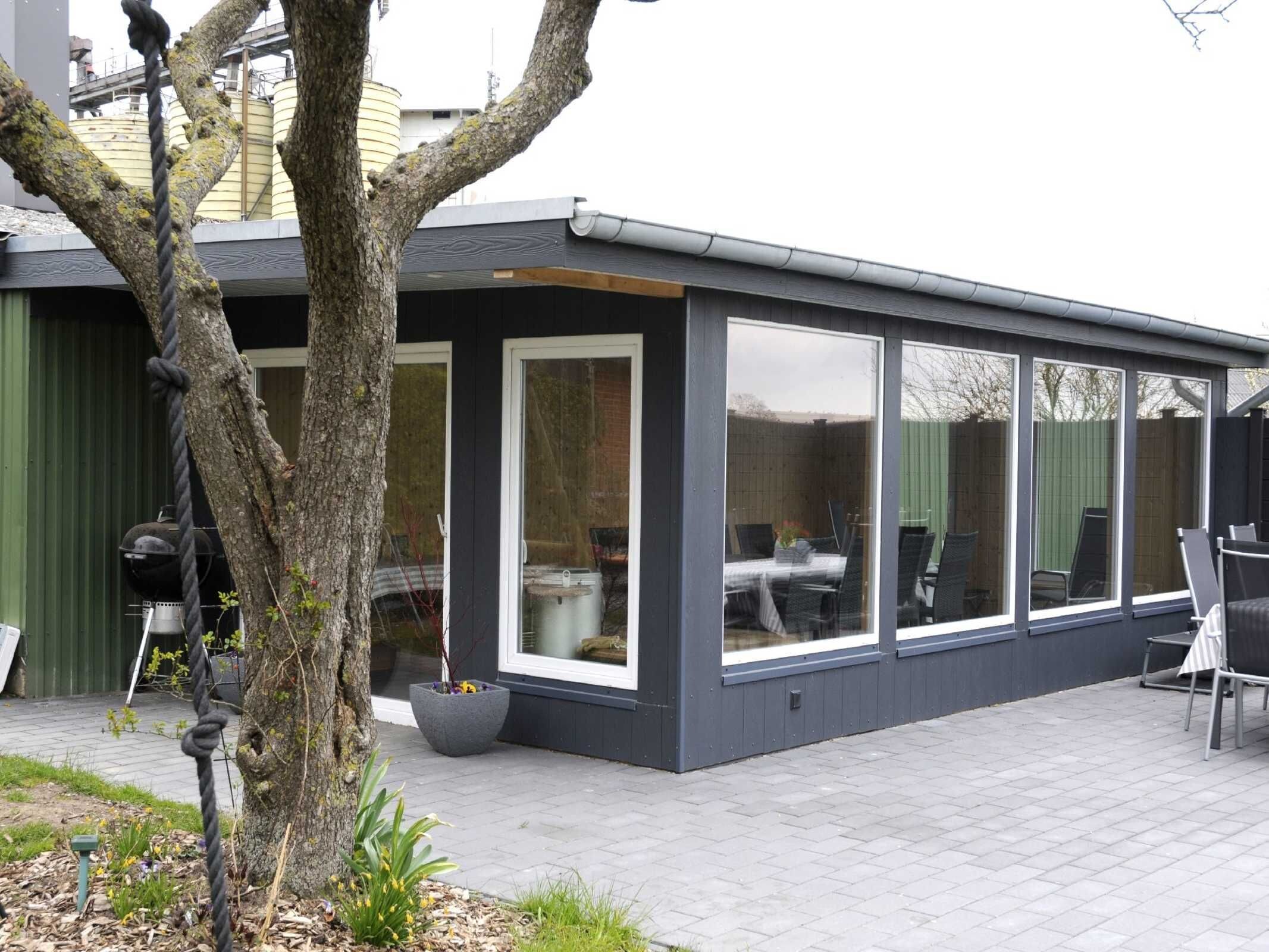Un edificio moderno con amplios ventanales, un patio y mobiliario exterior.
