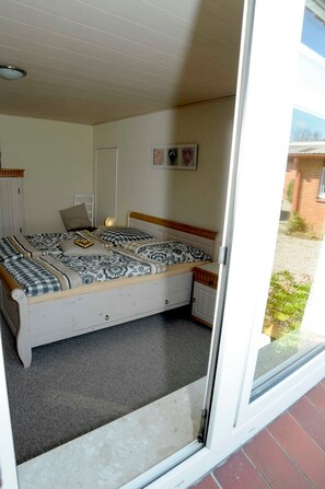 Ein Schlafzimmer mit einem Bett, einem Nachttisch, einem Heizkörper und einer Tür zu einem Außenbereich.
