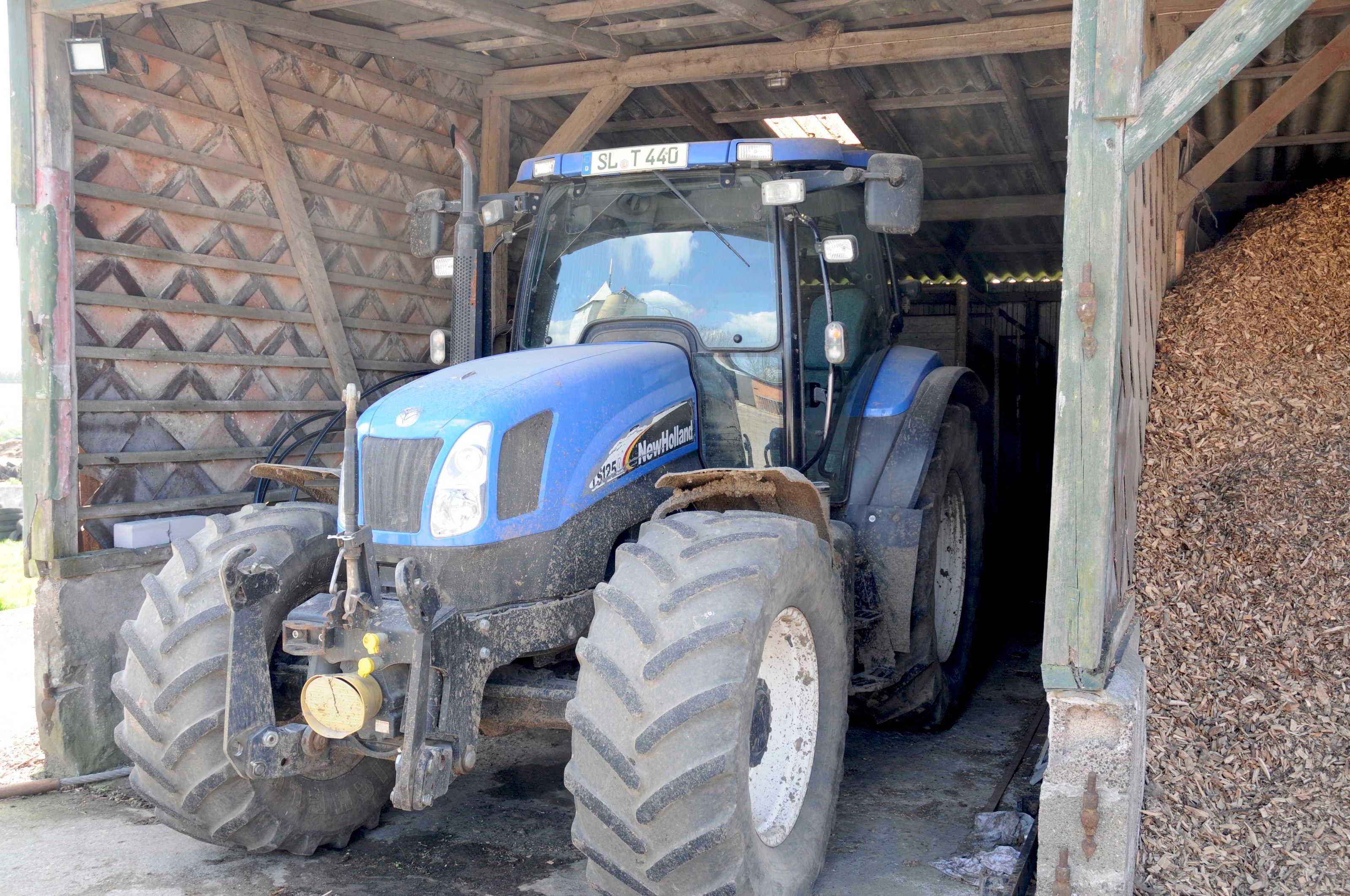 En blå traktor med store dæk parkeret inde i en trækonstruktion.