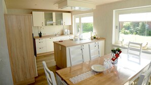 A modern kitchen with white cabinets, a wooden island, and a dining area with a table and chairs. - Vacation apartment Meer, Germany (Hasselberg)