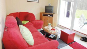 A living room with a red sofa, a small wooden cabinet, a television, and a glass door leading outside.