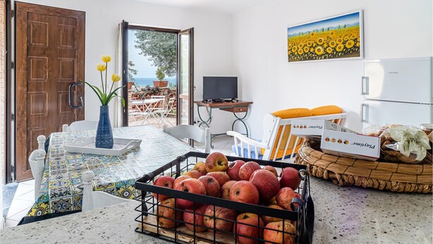 Una cocina con salpicadero de azulejos, una cesta de frutas, un televisor y un cuadro de girasoles.