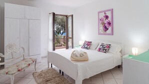 Un dormitorio con cama, mesita de noche, silla, armario y ventana con vistas al verde.