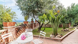 Un patio al aire libre con una mesa y sillas, rodeado de plantas en macetas y vistas al mar.