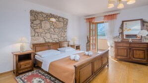 Un dormitorio con pared de piedra, cama de madera, lámparas de noche, una mesita de noche, cómoda y espejo, con vistas al exterior.