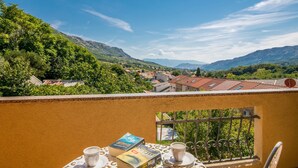 Un balcón con una mesa dispuesta para dos personas, con vistas a un pueblo de edificios con tejados rojos y colinas verdes al fondo.