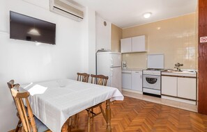 A compact kitchen with a dining area, including a table, chairs, a TV, and basic appliances.