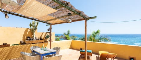Une terrasse meublée de mobilier en osier, avec une table et une chaise, donnant sur l’océan.