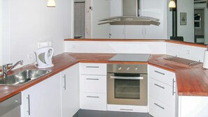 Eine kompakte Küche mit weißen Schränken, einer Edelstahl-Spüle, einem Backofen und einer Kaffeemaschine.