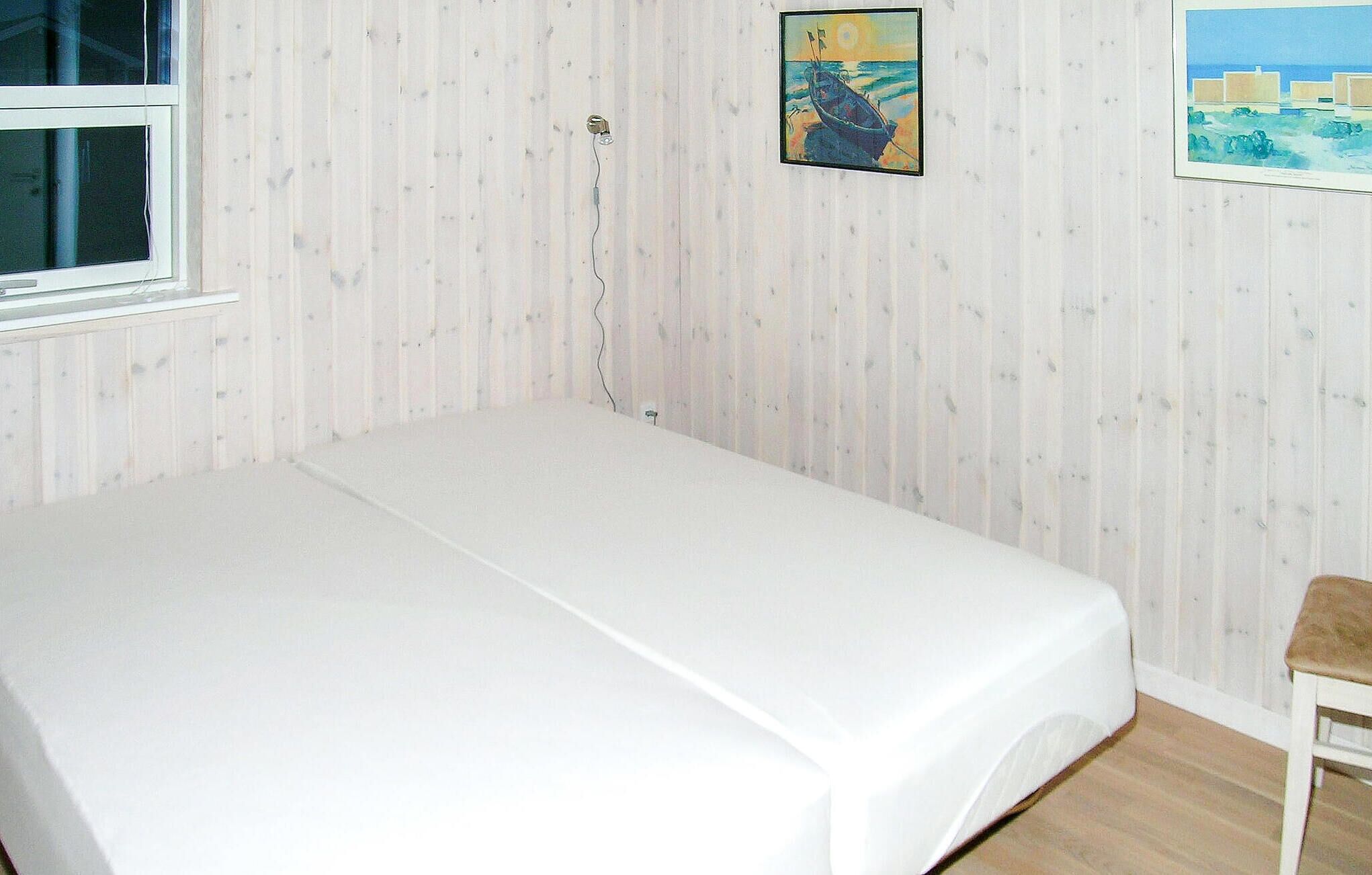 A room with a single bed, a window, and two paintings on the wall.