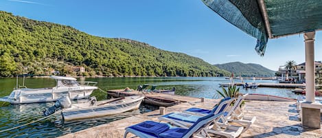 A marina with boats docked, lounge chairs, and a view of a lake surrounded by hills.