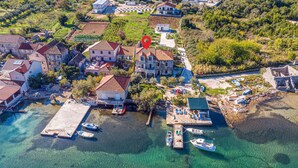 Une vue aérienne d’un village côtier, avec ses maisons, un quai où sont amarrés des bateaux et une promenade en bord de mer dégagée.
