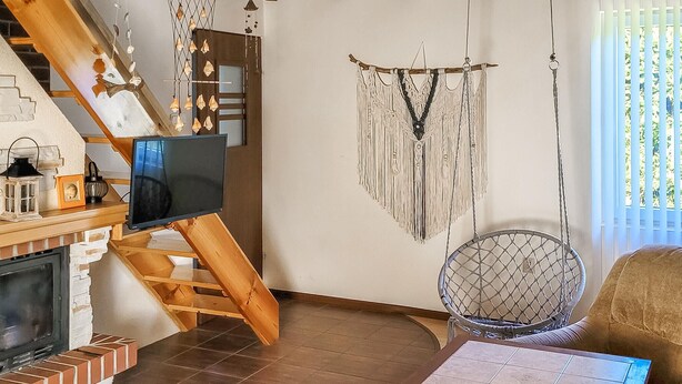 Una sala de estar acogedora con chimenea, televisor, un tapiz de macramé y una silla de mimbre.