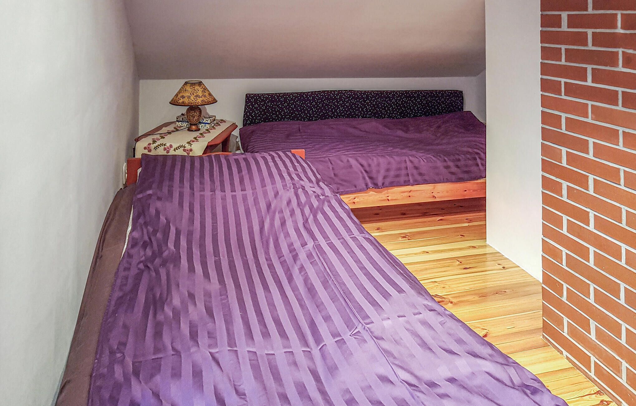 Una habitación pequeña con dos camas, una mesita de noche y una lámpara.