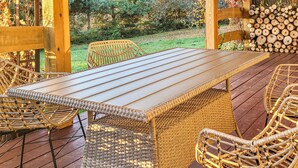 Una terraza de madera con una mesa larga y sillas de mimbre.