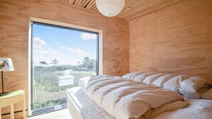 A bedroom with a large window, wooden walls, a bed with white bedding, and a small table with a lamp. - Amazing home in Ebeltoft with sauna (Ebeltoft)