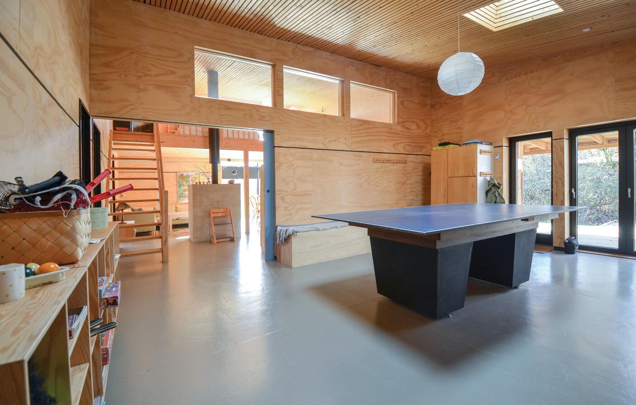 En rummelig stue med et ping pong bord, trævægge og store vinduer, der lukker naturligt lys ind.