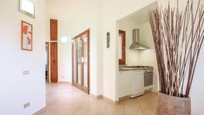A hallway leading to a kitchen with a stove, dishwasher, and a decorative vase with sticks.