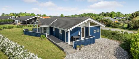 A blue house with a covered porch, a gravel driveway, and a grassy yard.