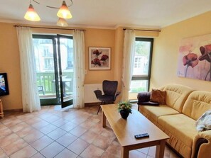 A living room with a sofa, a table, a chair, and a painting on the wall. - (213) 2-room apartment - apartment house Villa Laura (Kühlungsborn)
