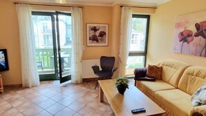 A living room with a sofa, a table, a chair, and a painting on the wall. - (213) 2-room apartment - apartment house Villa Laura (Kühlungsborn)
