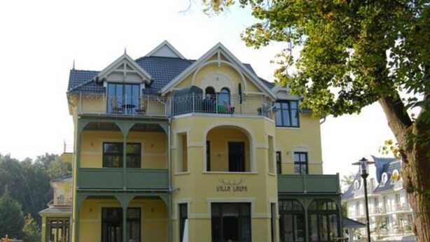 A multi-story building with balconies, a sign reading 'Hotel Lauma,' and a well-maintained garden area. - (213) 2-room apartment - apartment house Villa Laura (Kühlungsborn)