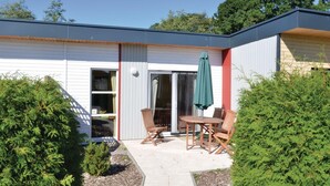 Una casa moderna con un patio, arredato con tavolo e sedie, immerso nel verde.